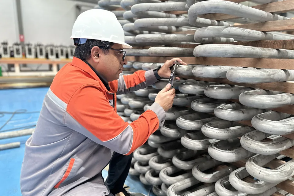 Arrow Energy engineer checking superheater coil U-bends with a digital caliper — SA-213 TP347H seamless tube, 50.8 mm OD × 5.5 mm wall, racked for coil assembly